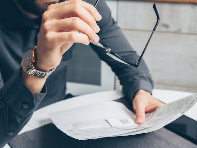 Person holding glases in one hand and a paper in the other